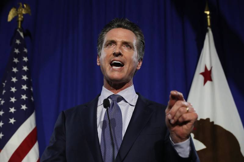 Gov. Gavin Newsom in a suit and tie speaks into a microphone