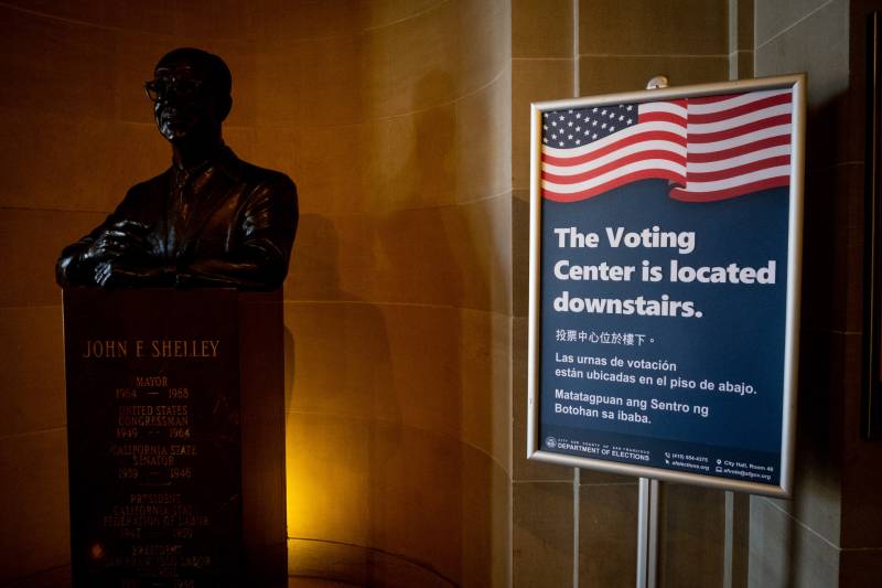 A sign in a dimly lit City Hall passageway reads "The Voting Center is located downstairs", next to a bronze bust of a man.