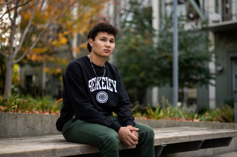 a young man sits on a concrete bench on a college campus