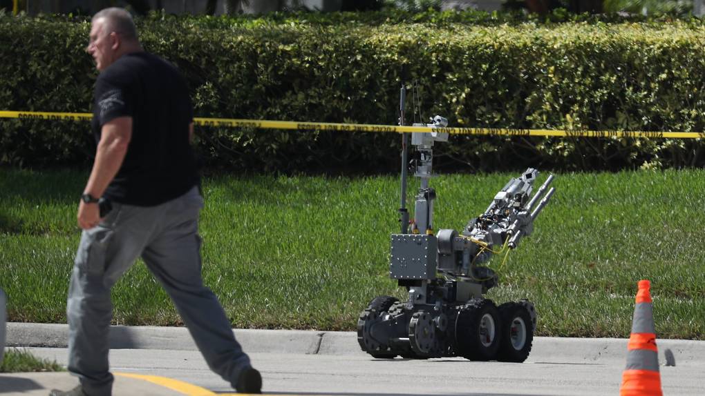 A walks dressed in a law enforcement uniform walks past a robot in the street.