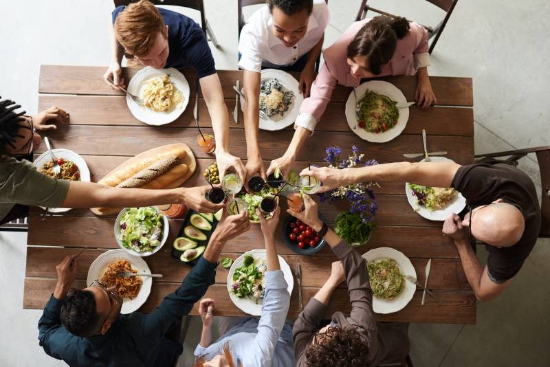 A shot taken from above of a group of people around a table, eating dinner and raising their glasses in a toast.