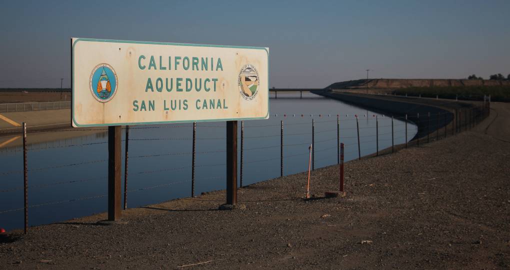 A water canal with a sign in front of it that reads "California Aquaduct - San Luis Canal"
