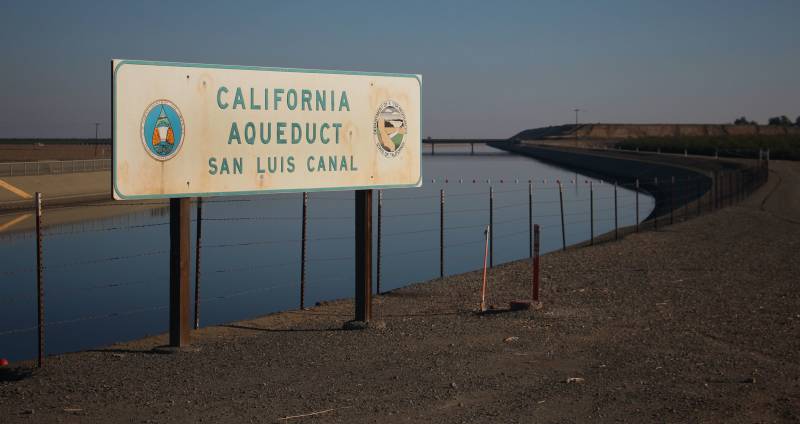 A water canal with a sign in front of it that reads "California Aquaduct - San Luis Canal"