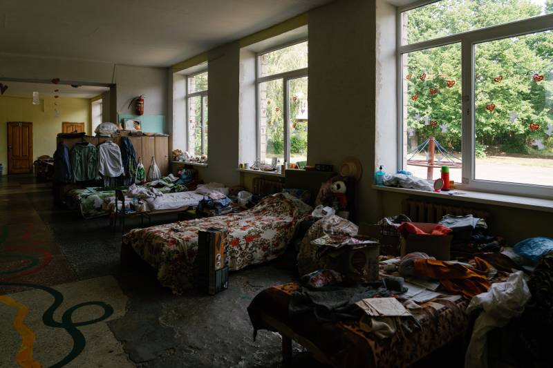 A long room filled with makeshift beds and cots, with personal belongings scattered about.