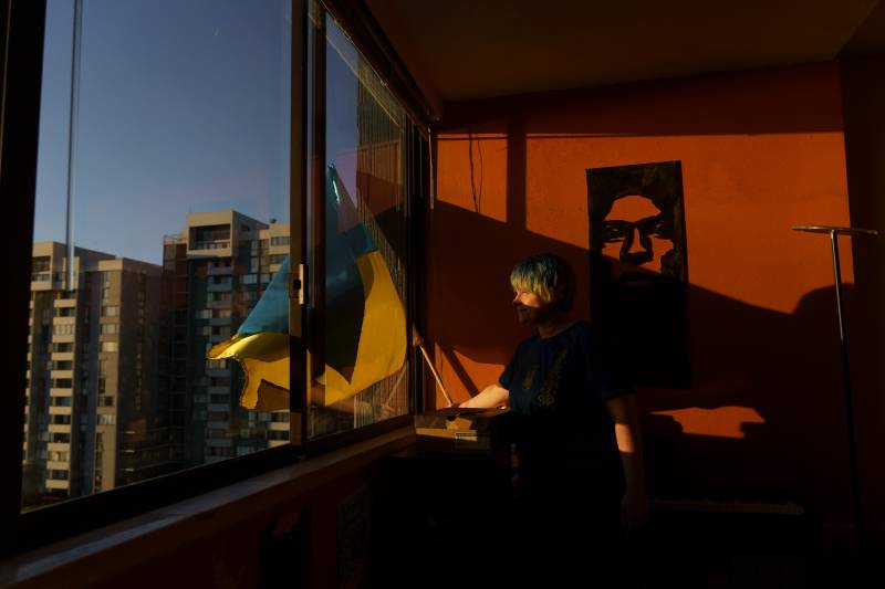 A woman hangs a Ukrainian flag out of an apartment window.