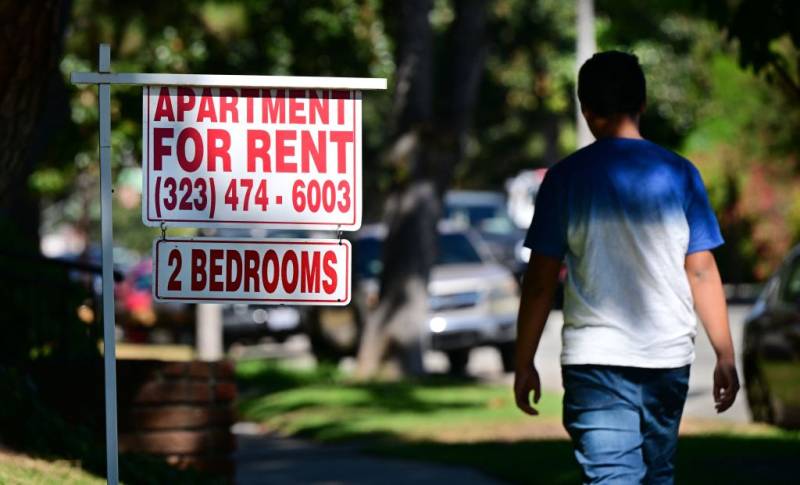 A sign that says "Apartment For Rent" with someone walking by.