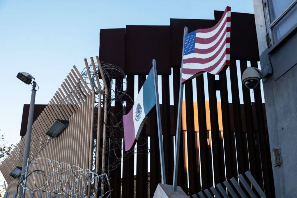 A view of a border with a Mexican and US flag and high steel barriers.
