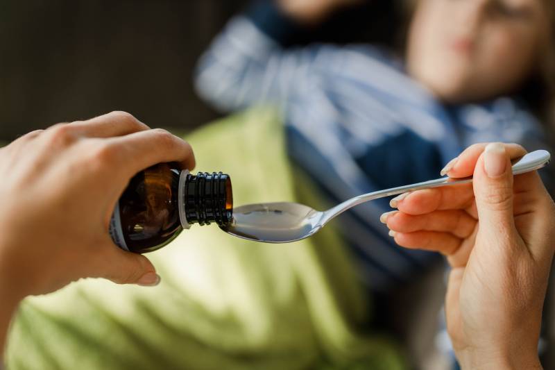 Close up of unrecognizable single mother pouring syrup into the spoon for her sick child.
