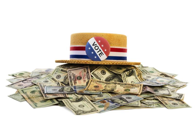 A hat with "Vote" written on it in red white and blue sits on top of a pile of bank notes.