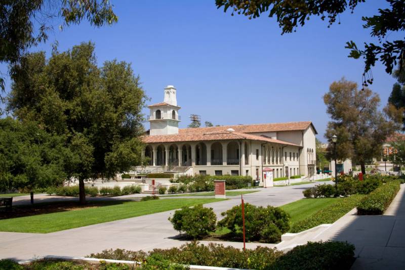 A white hacienda style building surrounded by prisine green lawns and paths on a college campus.