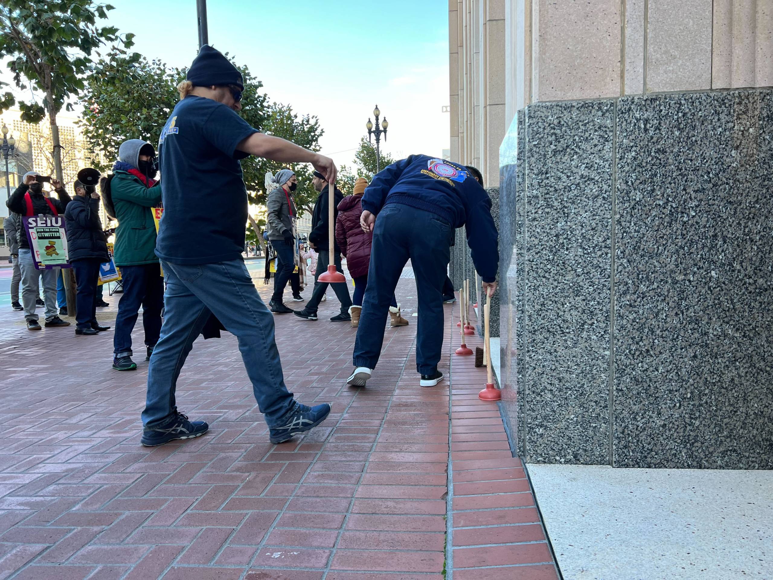Men place plungers and mops outside a building in downtown San Francisco.