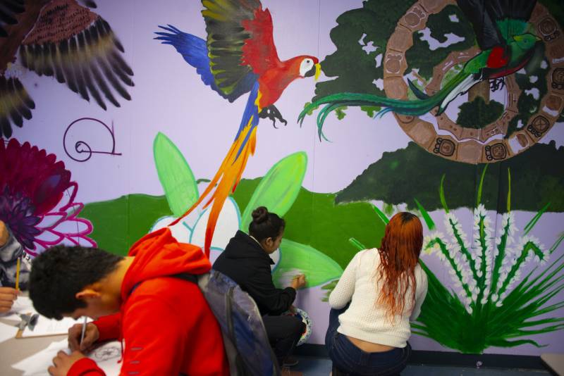 three high school students work on a colorful nature-inspired mural
