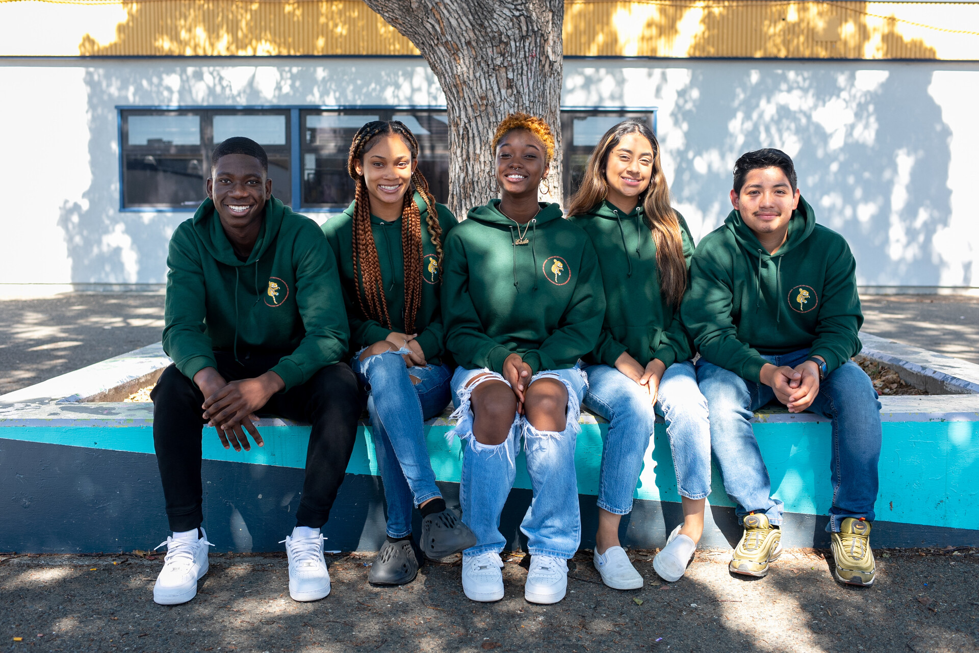 Five students sit side by side, a Black boy, two Black girls, a Latina girl, and a Latino boy.