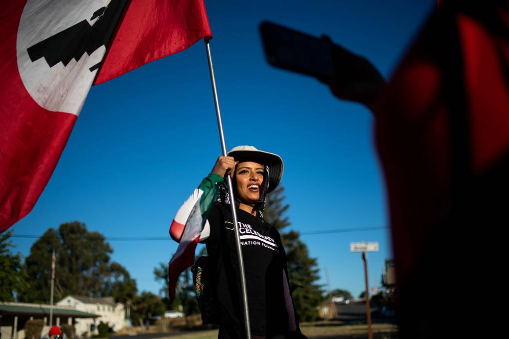 A young woman wearing a wide-brimmed hat smiles and carries a flag aloft
