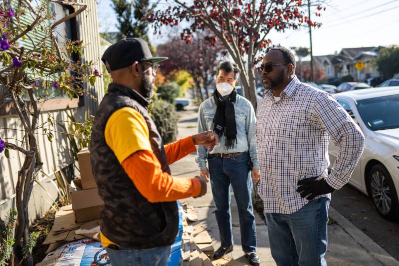 Two Black men talk on a neighborhood street.