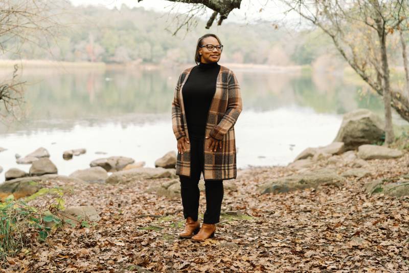 A Black woman with glasses standing in a park.