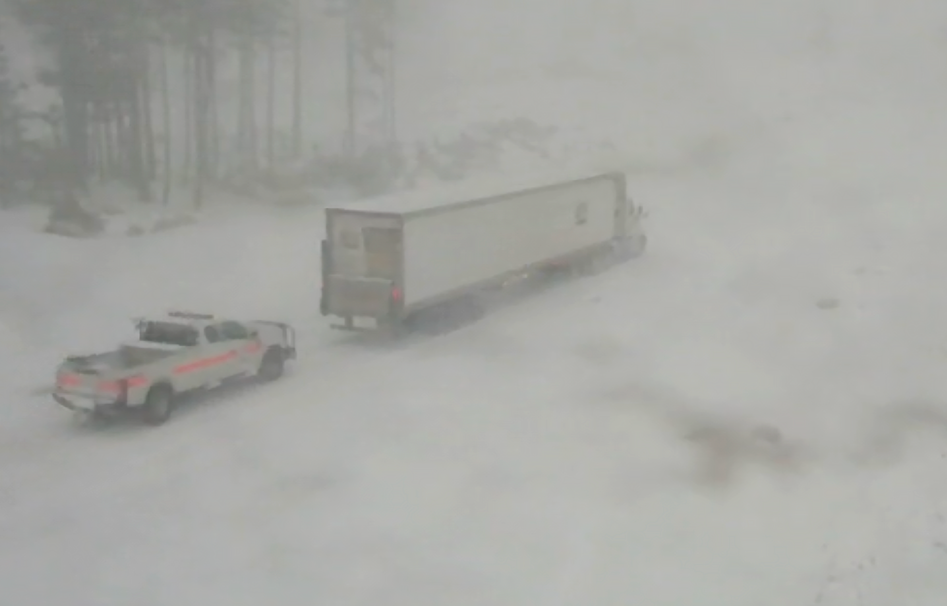 A screenshot of trucks driving through the snowy conditions on the road.