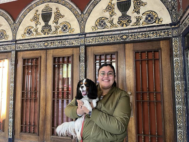 a woman in a green jacket poses with her dog in front of a historic movie theater
