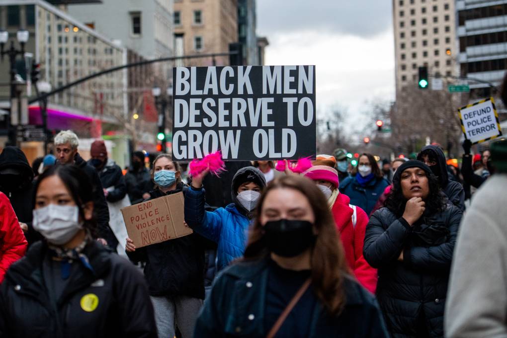 A person in a crowd of people in the street holding a sign that reads "Black men deserve to grow old."