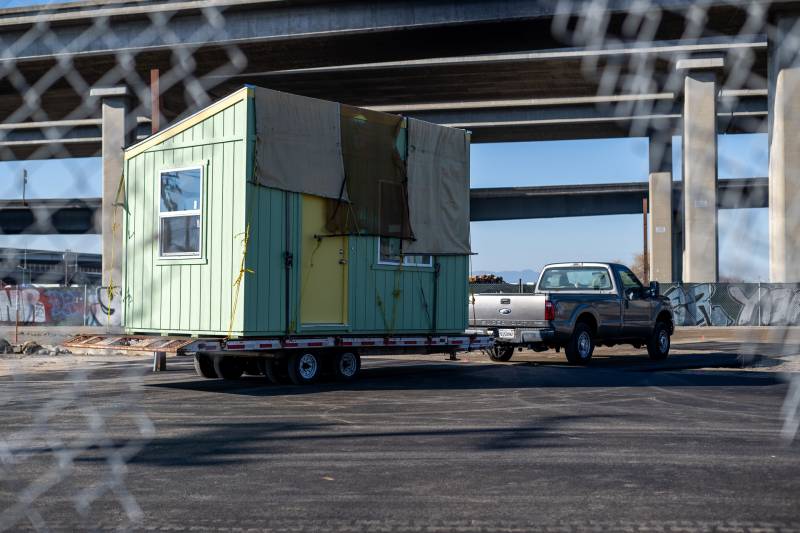 A pale green tiny home is seen attached to a truck outside.