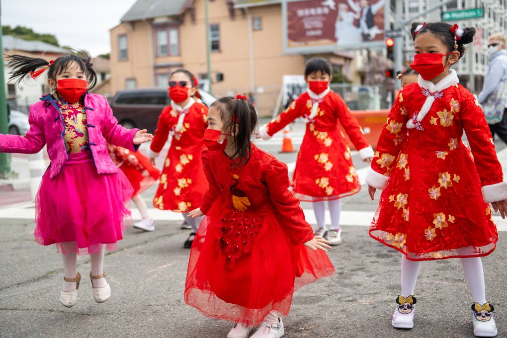 Young asian girls in red dresses with one girl wearing a pink dress pose outside on the street.