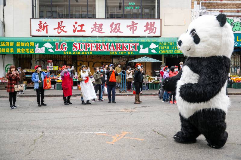 A person in a panda costume walks down the street with other people on the side.