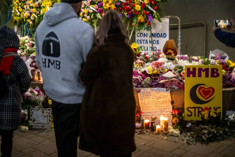 A man and a woman seen from behind as they look at an altar with flowers and candles.