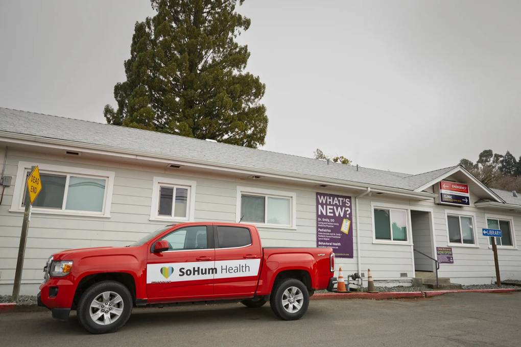 A red truck with "SoHum Health" written on the side is parked outside a one-story white hospital building.