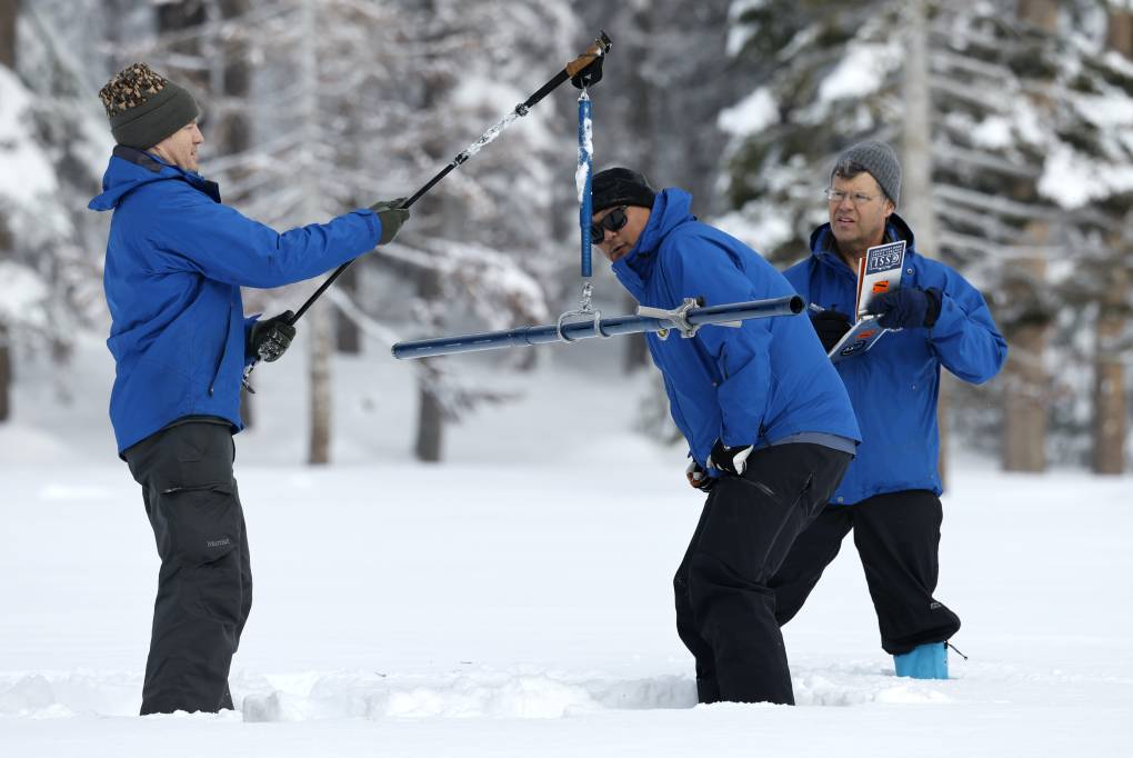 Three people dressed in blue and black measure snow