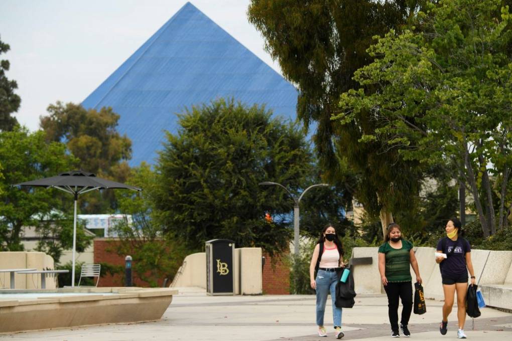 Three students walk on campus with trees around them and the tip of a dark glass pyramid in the background.