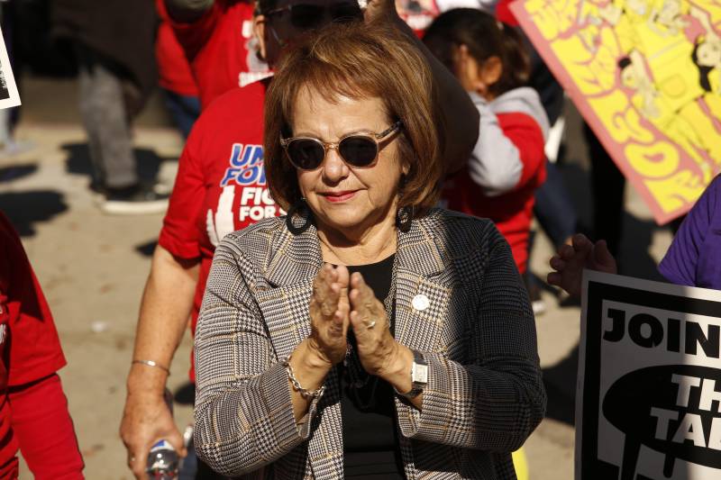 a woman in a blazer and sunglasses is seen clapping outside at a protest