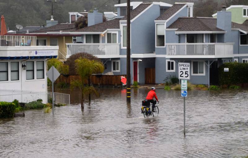 A flooded city neighborhood with a man riding by on a road bike.