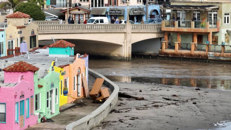 A view of damaged colorful houses along the shores of the river with a bridge in Capitola.