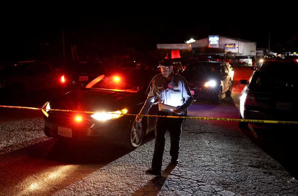 A police officer patrols an area at night that's cordoned off with caution tape.
