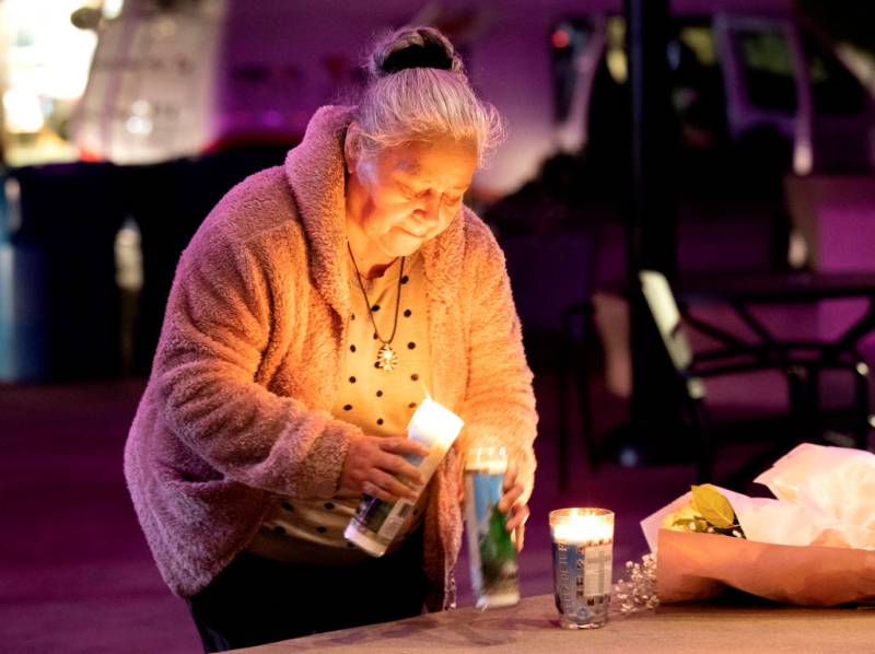 An elderly Latina woman lights a candle at a memorial