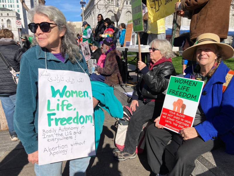 Two women hold signs that read "women life freedom" and "women for freedom"