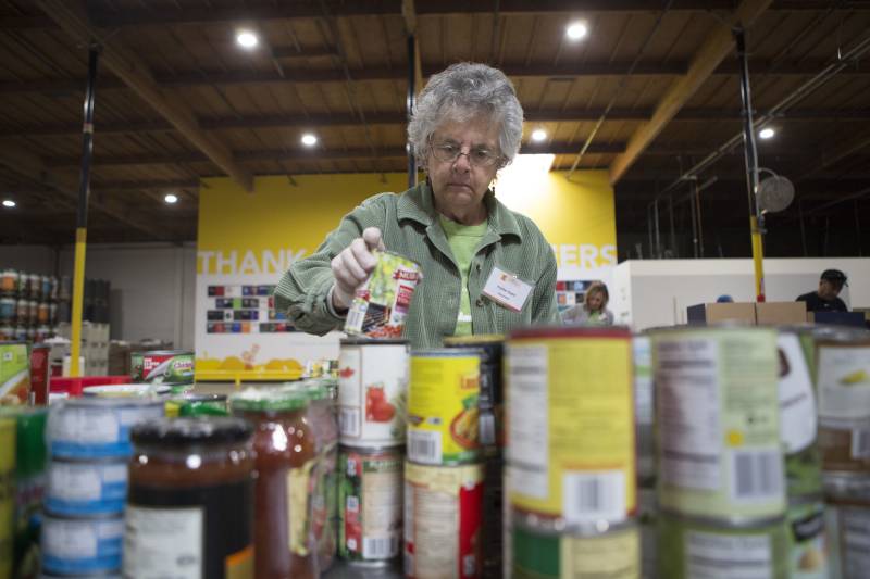 An elderly white woman sorts through canned food.