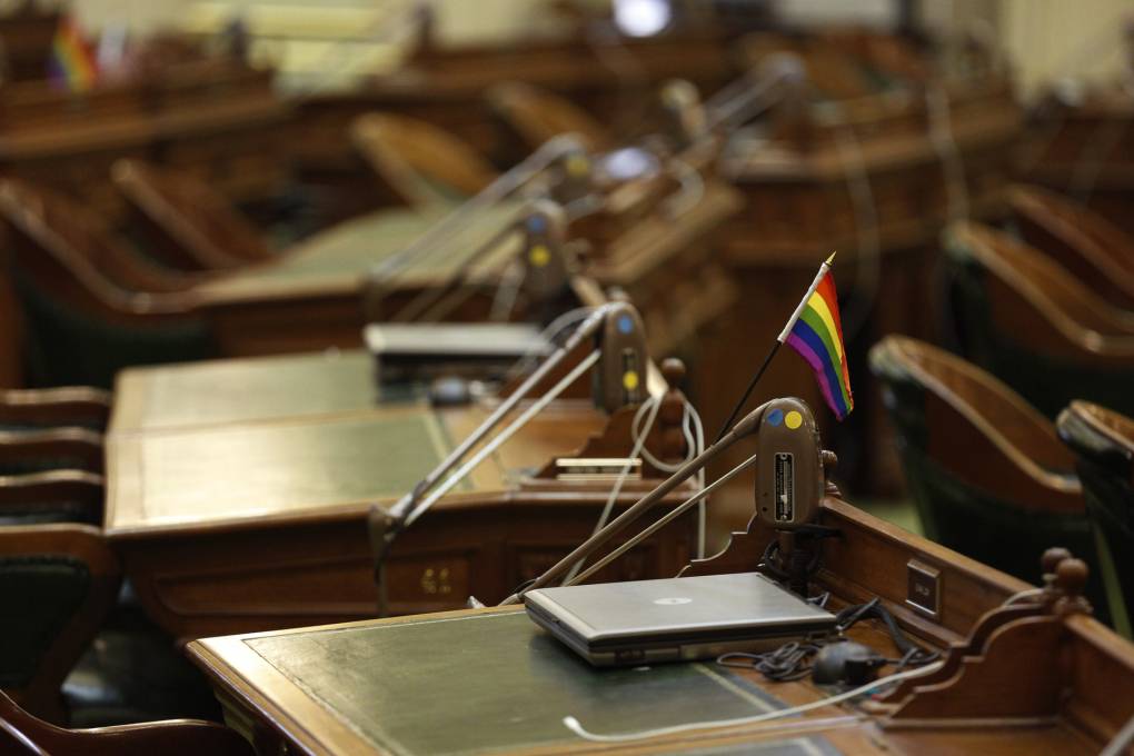 Empty Assembly desks with a small LGBTQ flag on one of the desks.