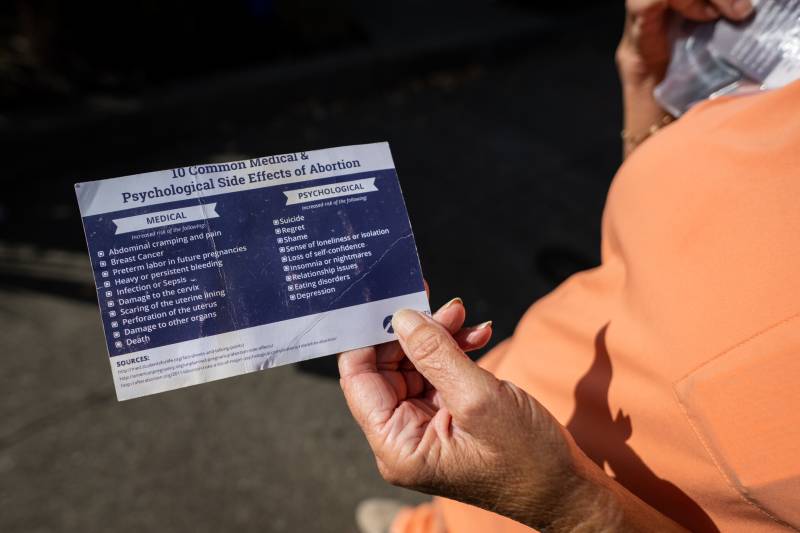 The hand of an older white woman holds a pamphlet describing inaccurate side effects of abortions