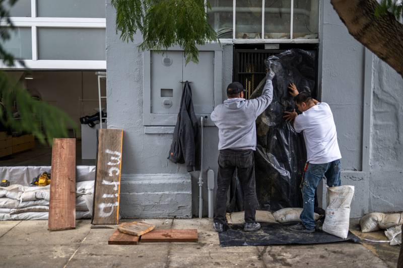 Two men putting up sandbags in front of a door in a an urban neighborhood.