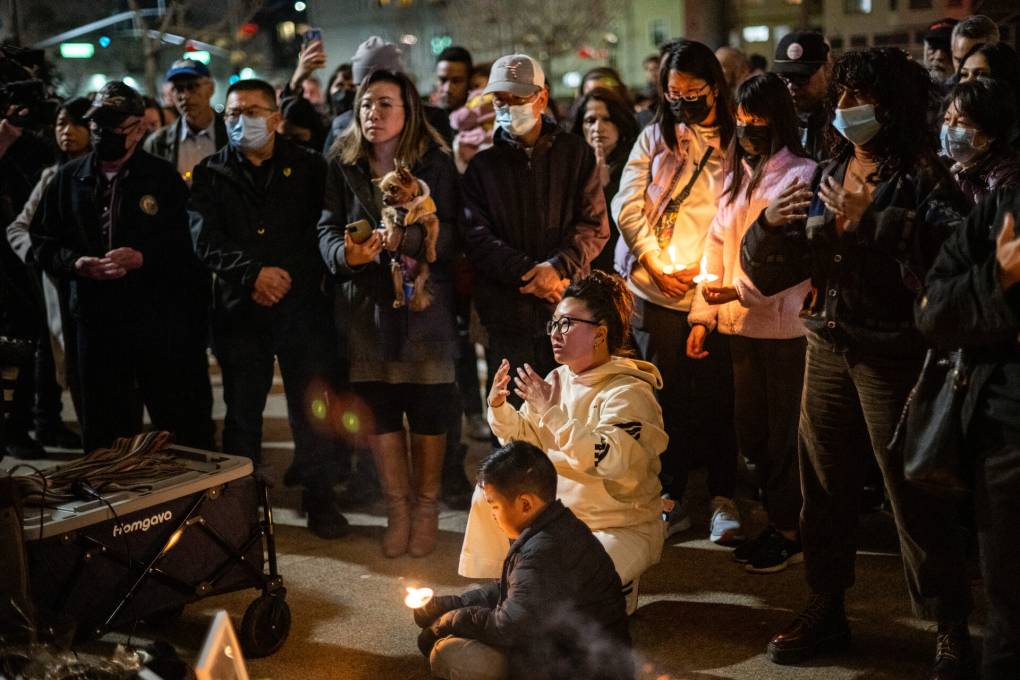 A group of people stand outside with some people crouching and sitting while holding a candle.