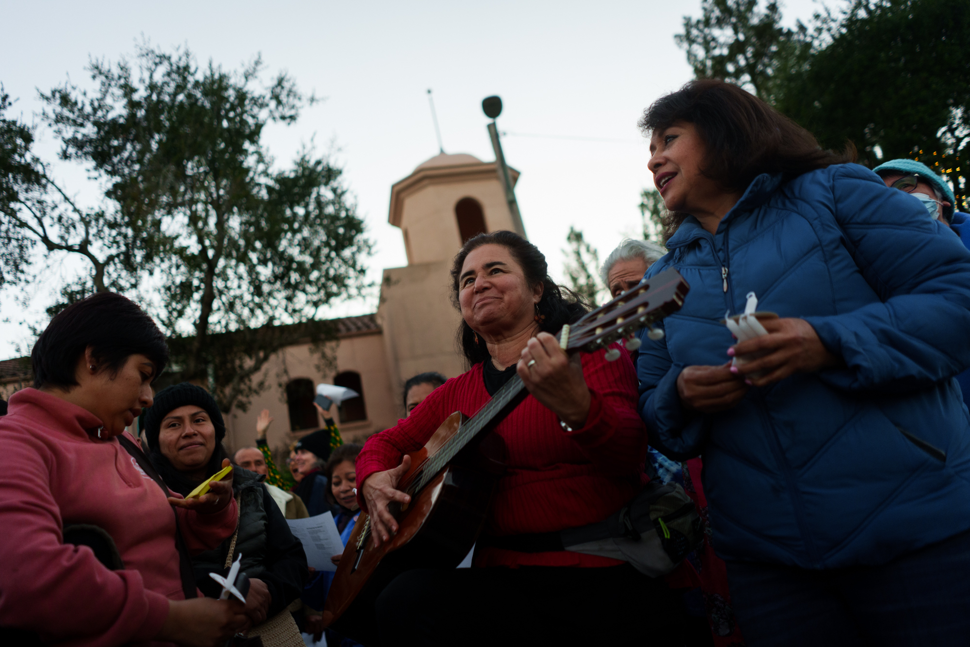 A woman plays guitar while standing outside among a crowd of demonstrators.