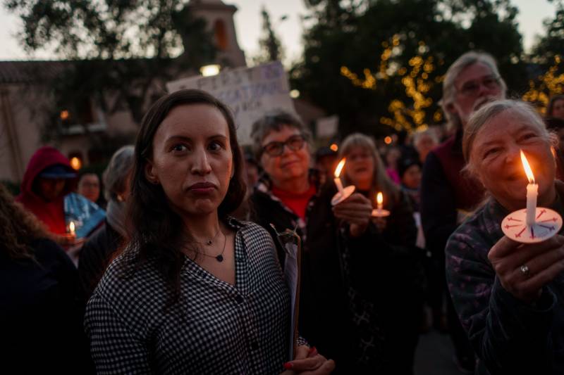 A crowd of people hold candles outside at dusk.