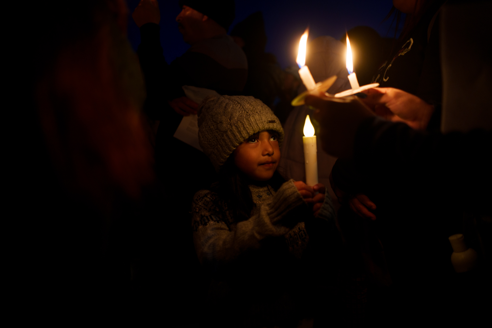 A young girl holds a candle outside in the dark.