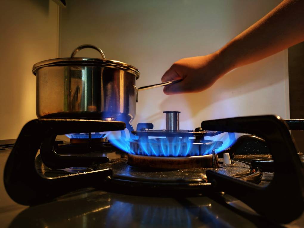 A woman's hand holds a pot over a blue flame from a gas stove.