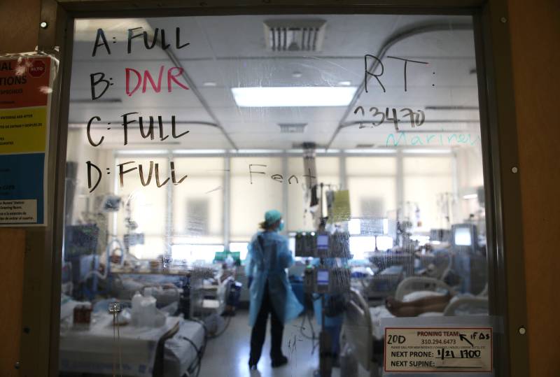 In the background is a clinician with patients in an ICU unit. In the foreground is a glass window that indicates the area is full of patients.