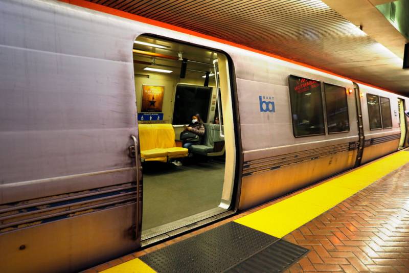 A BART train at a platform with sliding doors open and a passenger sitting inside.