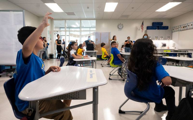 Students in a classroom, one student raises a hand.