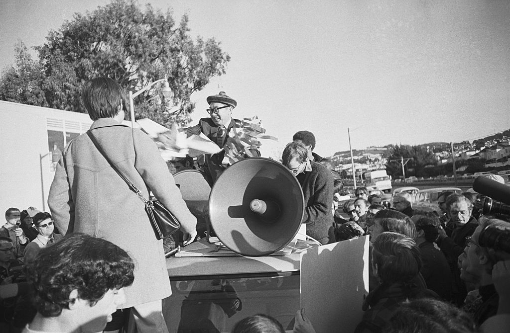 A man in a hat rips out wires behind a bullhorn. 