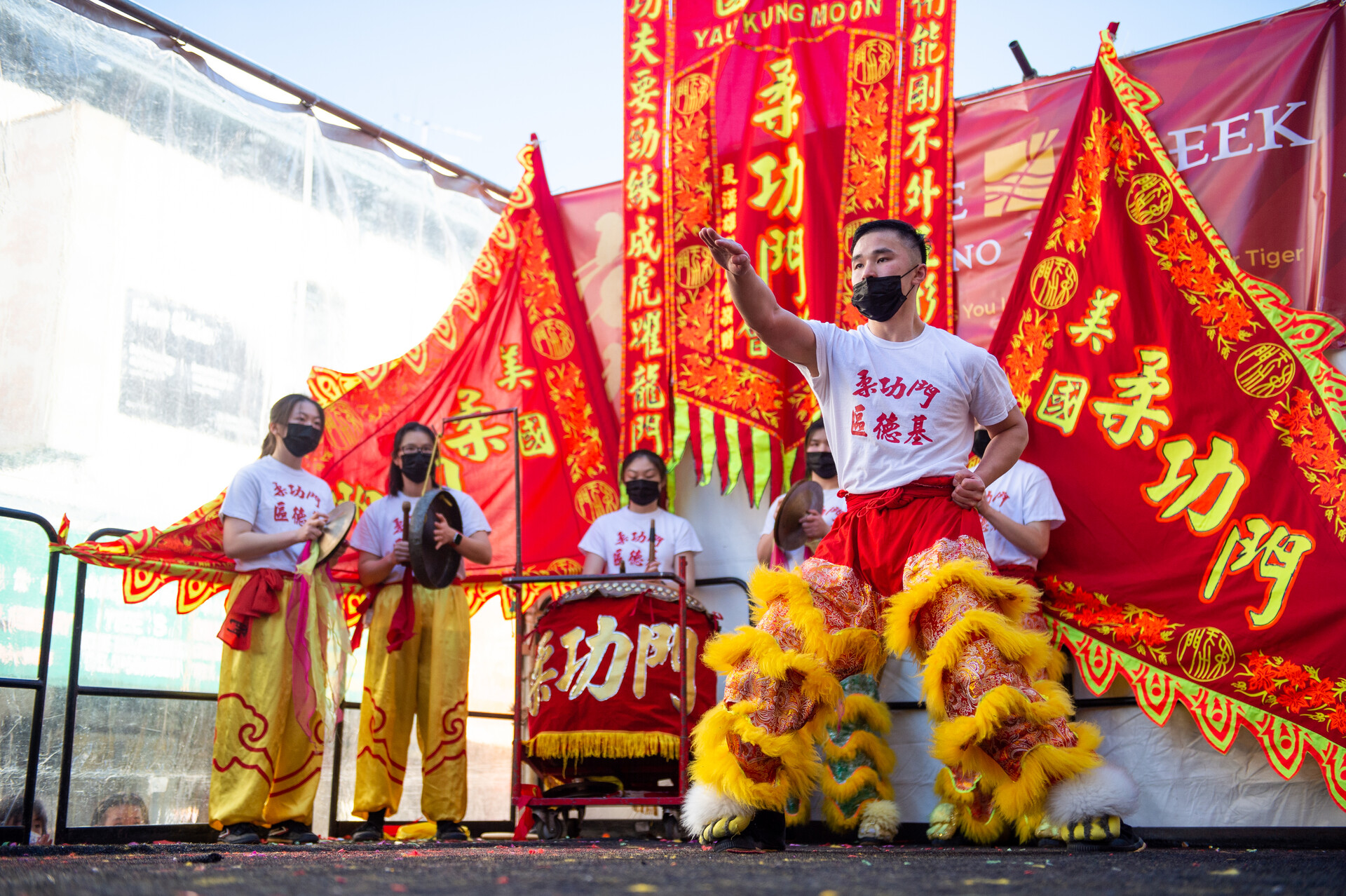 man wearing white and red shirt, traditional bright yellow and red leggings, performs a kung fu form on an outdoor stage